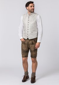 Traditionelles Männeroutfit mit einem gemusterten hellgrauen Weste und braunen Lederhosen mit dekorativer Stickerei, kombiniert mit knielangen Socken und braunen Schuhen.