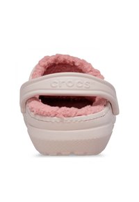 Roze, met fleece gevoerde Crocs met een witte buitenkant en een achterband, voorzien van een gestructureerde zool en zichtbare stikdetails.