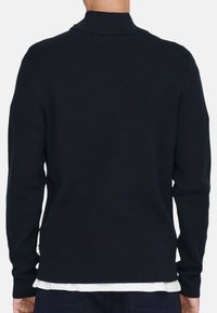 Pull en tricot noir à côtes avec un col montant, des manches longues et une coupe ajustée. Comprend un détail de ourlet superposé en bas.