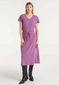 Vestido de punto de manga corta y escote en V en un vibrante color lavanda, ceñido a la cintura con un lazo, combinado con botas de cuero negras hasta la rodilla.