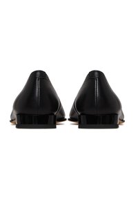 Chaussures en cuir noir avec un petit talon rectangulaire, texture lisse et design minimaliste, présentant des lignes courbes au niveau du talon et à l'arrière.