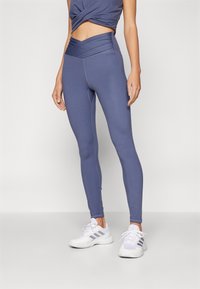 Leggings in tessuto morbido e elastico, con vita alta e un design a strati in un colore blu tenue. Dettagli delle cuciture sono visibili.