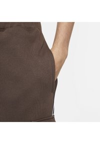 Brunt stickad klädsel med sidficka, texturerad tyg och kontrasterande sidodetaljer i vitt. Närbild som framhäver designens detaljer.