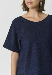 Tricou bleu marin, cu mânecă scurtă, realizat dintr-un material texturat și strălucitor, cu decolteu larg și rotund, având o croială confortabilă.
