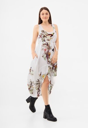 Largo vestido blanco con estampado floral en varios colores, con una cintura anudada y abertura lateral. Combinado con botas negras hasta el tobillo.