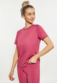 Růžové sportovní tričko z lehkého, hladkého materiálu s krátkými rukávy a kulatým výstřihem, nošené s odpovídajícími legínami.