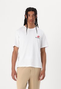 Witte katoenen T-shirt met korte mouwen, met een kleine rode aardbei grafiek en zwarte tekst op de linkerkant van de borst.