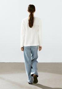 Bílý upravený blazer s dlouhými rukávy, spárovaný se světle modrými kalhotami širokého střihu. Hladká textura, jednoduchý design a žádné viditelné vzory.