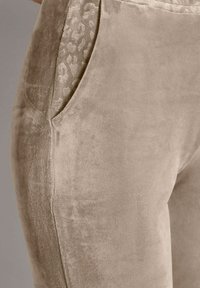 Weiche beige Sweatpants mit einer glatten Textur, die eine Seitentasche mit einem dezenten Leopardenmuster aufweist.