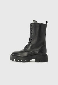 Botas negras de cuero con cordones y suela gruesa, acabado ligeramente texturizado y lengüeta en la parte posterior. Presenta ojales prominentes y costuras.