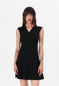 Musta hihaton mekko V-päällä, tiukka bodice ja levenevä hame. Valmistettu sileästä kankaasta, jossa on hienovaraista ompelusaumakuviota.