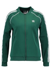 Zelená bunda na zip z bavlněné směsi. Má bílé pruhy na ramenou a rukávech, boční kapsy a malý logo na hrudi.