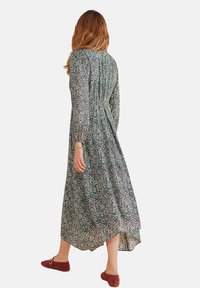 Maxikleid mit grünem Blumenmuster, langen Ärmeln und taillierter Taille. Hergestellt aus leichtem Stoff, hat es einen asymmetrischen Saum.