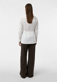 Koszula w paski w białym i pastelowych kolorach z wcięciem w talii, zestawiona z szerokimi, ciemnobrązowymi spodniami. Gładka tekstura, casualowy krój.