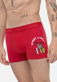 Boxers de algodón rojos con un diseño gráfico que presenta piernas de bastón de caramelo verdes y blancas y regalos. El texto dice "NO SOY UN SANTA."