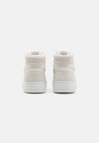 Wysokie sneakersy w jasnobeżowym zamszu i skórze, z gładkim wykończeniem, wyściełanym kołnierzem oraz białą gumową podeszwą z minimalnymi detalami.