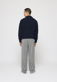 Pulover tricotat de culoare bleumarin, cu guler tip șal și mâneci lungi, asortat cu pantaloni largi de culoare gri deschis. Textură de țesătură netedă și o croială relaxată.