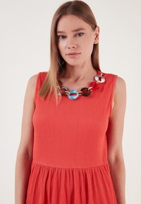 Rotes, strukturiertes Kleid mit ausgestelltem Rock, kombiniert mit einer bunten Statementkette mit runden Gliedern in Blau, Rot und Braun.