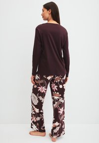 Donkerpaarse top met lange mouwen gecombineerd met broek met bloemenpatroon in tinten crème, roze en bruin, met een ontspannen pasvorm en wijde pijpen.