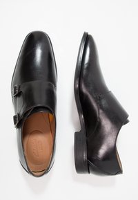 Chaussures habillées en cuir noir avec un bout arrondi et deux boucles en accent. Texture lisse, petit talon et doublure intérieure beige.