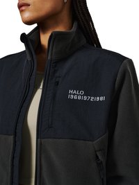 Kvinde iført en sort fleecejakke med "HALO 196819721981" trykt over en lynlåslomme på brystet.
