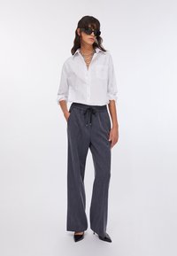 Chemise blanche à boutons avec des rayures verticales subtiles, associée à un pantalon large à fines rayures foncé avec une taille élastique et un cordon de serrage.