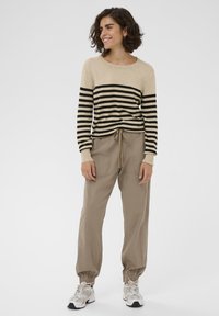 Beige stribet sweater med sorte vandrette striber, kombineret med lysebrune bukser med snører, elastiske manchetter og to forlommer.