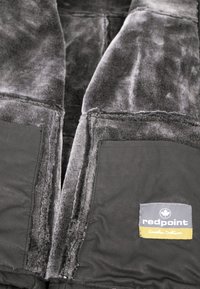 Schwarze Jacke mit einem weichen grauen Fleece-Futter, ausgestattet mit großen Taschen und einem sichtbaren Etikett. Es gibt einen Reißverschluss und strukturierte Stoffdetails.