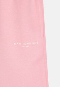 Rosa bomullstyg med en текстurerad yta och en vit logotyp som läser "TOMMY HILFIGER EST. 1985" nära mitten. Enkelt och rent design.