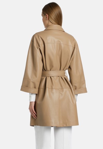 Tan læderjakke med bælte, der har brede ærmer og rygplade. Den glatte tekstur fremhæver det skræddersyede design.