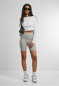 Camicetta bianca a maniche lunghe tagliata, pantaloni corti grigi a vita alta e sneakers bianche con dettagli neri. Occhiali da sole neri e borsa nera.