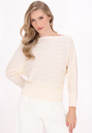 Crème kleurige gebreide trui met een horizontale streeptextuur, brede boatneck en ribgebreide manchetten. Gecombineerd met lichte broek.