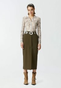 Blusa con base beige chiaro e motivo astratto marrone, abbinata a una gonna alta oliva e stivali da cowboy marroni con hardware argentato.