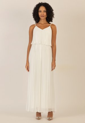 Weißes, plissiertes Maxikleid mit verstellbaren Spaghetti-Trägern, V-Ausschnitt und geschichteter Gestaltung. Sanfte Textur, bodenlang, kombiniert mit verzierten Absätzen.