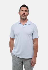 T-shirt polo bleu clair à manches courtes, avec un col plat et une texture lisse. Porté avec un pantalon léger gris à rayures.