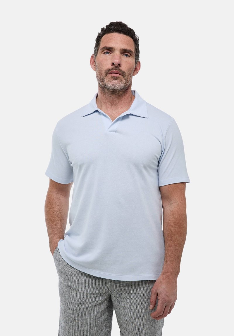 T-shirt polo bleu clair à manches courtes, avec un col plat et une texture lisse. Porté avec un pantalon léger gris à rayures.