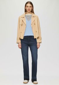 Beige, doppelt geknöpfter Blazer, hellblauer Pullover, gestreiftes Oberteil, dunkle Jeans, helle Sneakers mit dicker Sohle und durchgehenden Zehenakzenten.