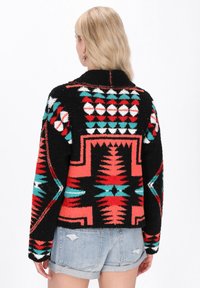 Zwarte, gestructureerde trui met levendige patronen in rood, turquoise en wit. Heeft een kraag en een cropdesign met brede mouwen.