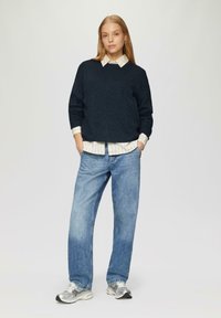 Marineblauwe gebreide trui met een gestructureerd oppervlak, gedragen over een witgestreept shirt. Gepaard met lichtblauwe denim jeans en zilveren sneakers.