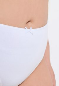 Witte katoen onderbroeken met een gladde textuur, voorzien van een klein wit strikaccent op de tailleband. Close-upweergave toont de pasvorm en ontwerpdetails.