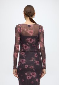 Διαφανές μαύρο τοπ με μακριά μανίκια, διακοσμημένο με λουλουδένιο σχέδιο σε αποχρώσεις του ροζ και του πράσινου, με στρογγυλή λαιμόκοψη και τελείωμα με βολάν.