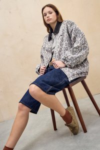 Jaqueta de denim com padrão de leopardo, punhos elásticos, blusa cinza, calções de denim azuis e meias castanhas, combinando com sapatos mocassins verdes.