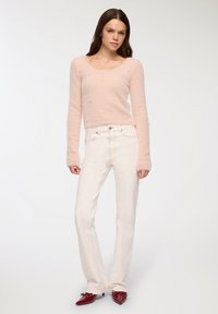 Jasnoróżowy, puszysty sweter z małymi, wypukłymi akcentami w połączeniu z białymi dżinsami o prostych nogawkach oraz czerwonymi, spiczastymi butami.