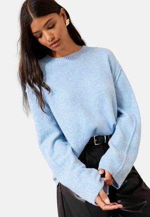Hellblauer gestrickter Pullover mit Rundhalsausschnitt, überschnittenen Schultern und gerippten Bündchen, kombiniert mit hoch taillierten schwarzen Lederhosen.