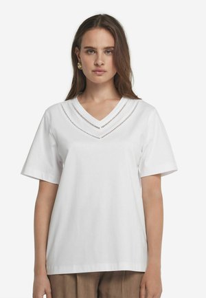 Weißes Baumwoll-T-Shirt mit kurzen Ärmeln, V-Ausschnitt und dekorativen Ausschnitten entlang des Ausschnitts. Glatte Textur und lässige Passform.