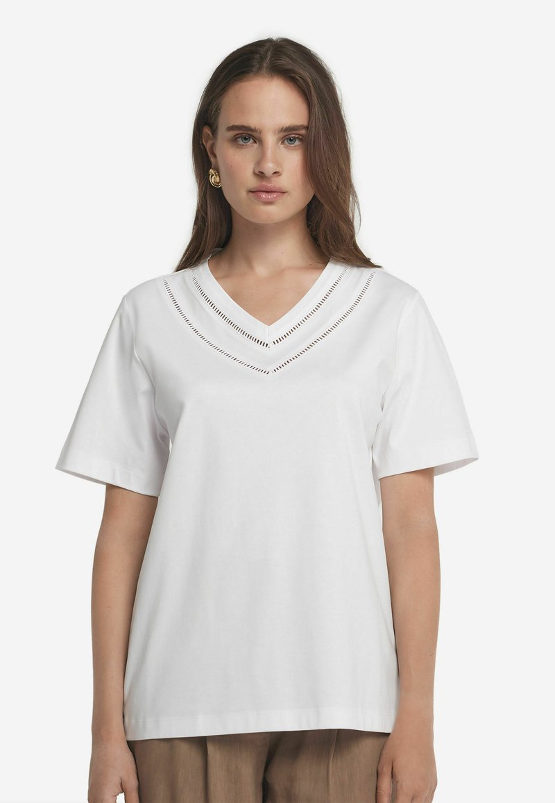 Hvid bomulds T-shirt med korte ærmer, V-halsudskæring og dekorative udskæringer langs halsudskæringen. Glat overflade og afslappet pasform.