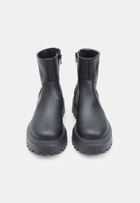 Crne gležnjače od glatke kože s dvostrukim bočnim patentnim zatvaračima, čvrstim gumenim potplatima i zaobljenim vrhom.