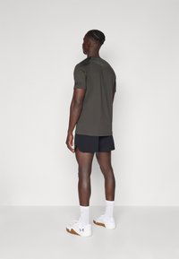 Camisa masculina de manga curta verde-escura com gola redonda, combinada com calções pretos e ténis brancos. Design e ajuste simples.