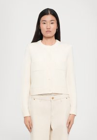 Korthvid cardigan med ribbet tekstur, rund halslinje og knappelukking. Har to frontlommer og lange ermer.