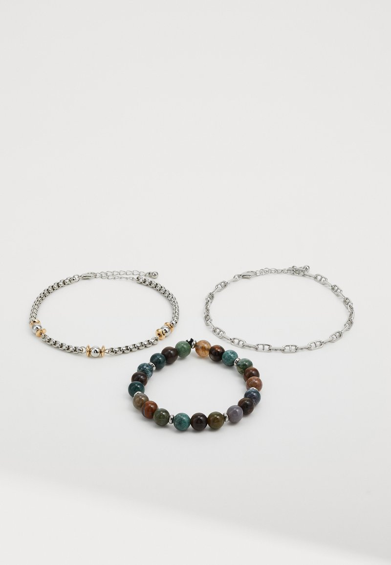 Trois bracelets : chaîne en argent avec accents dorés, chaîne en maillons argentés et bracelet en perles dans des teintes vertes, brunes et bleues.